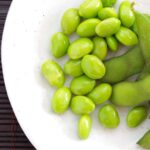 Is edamame keto? with shelled and non-shelled edamame on a white plate