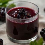 Juicing elderberries in a glass with berries on top
